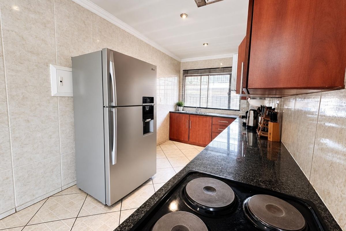 A functional kitchen featuring granite countertops, dark wood cabinetry, tiled walls, and a built-in electric hob with an overhead extractor fan.