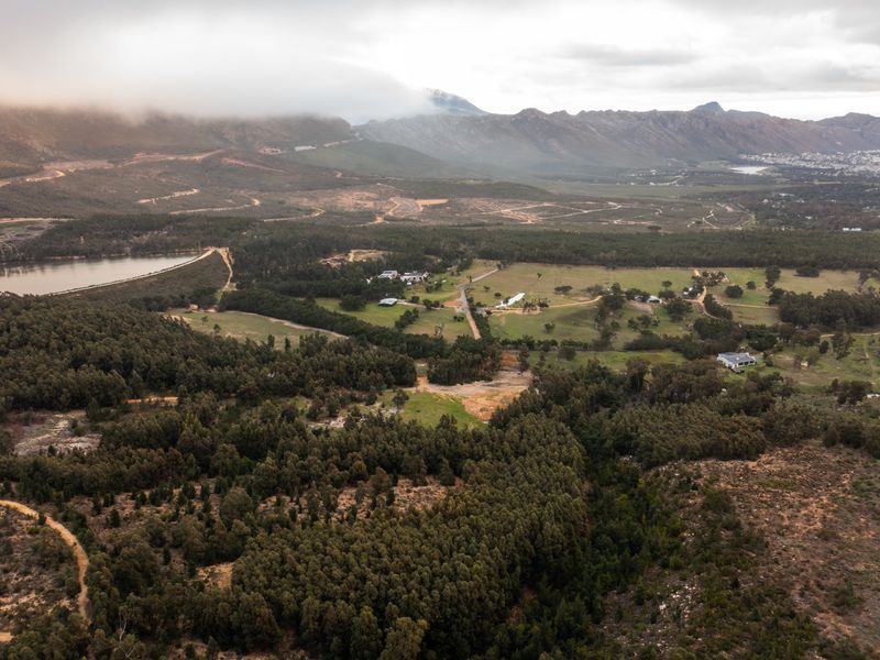 An expansive aerial view of the farm property, showcasing the surrounding forest, open pasture land, private dam, and scenic mountain backdrop.