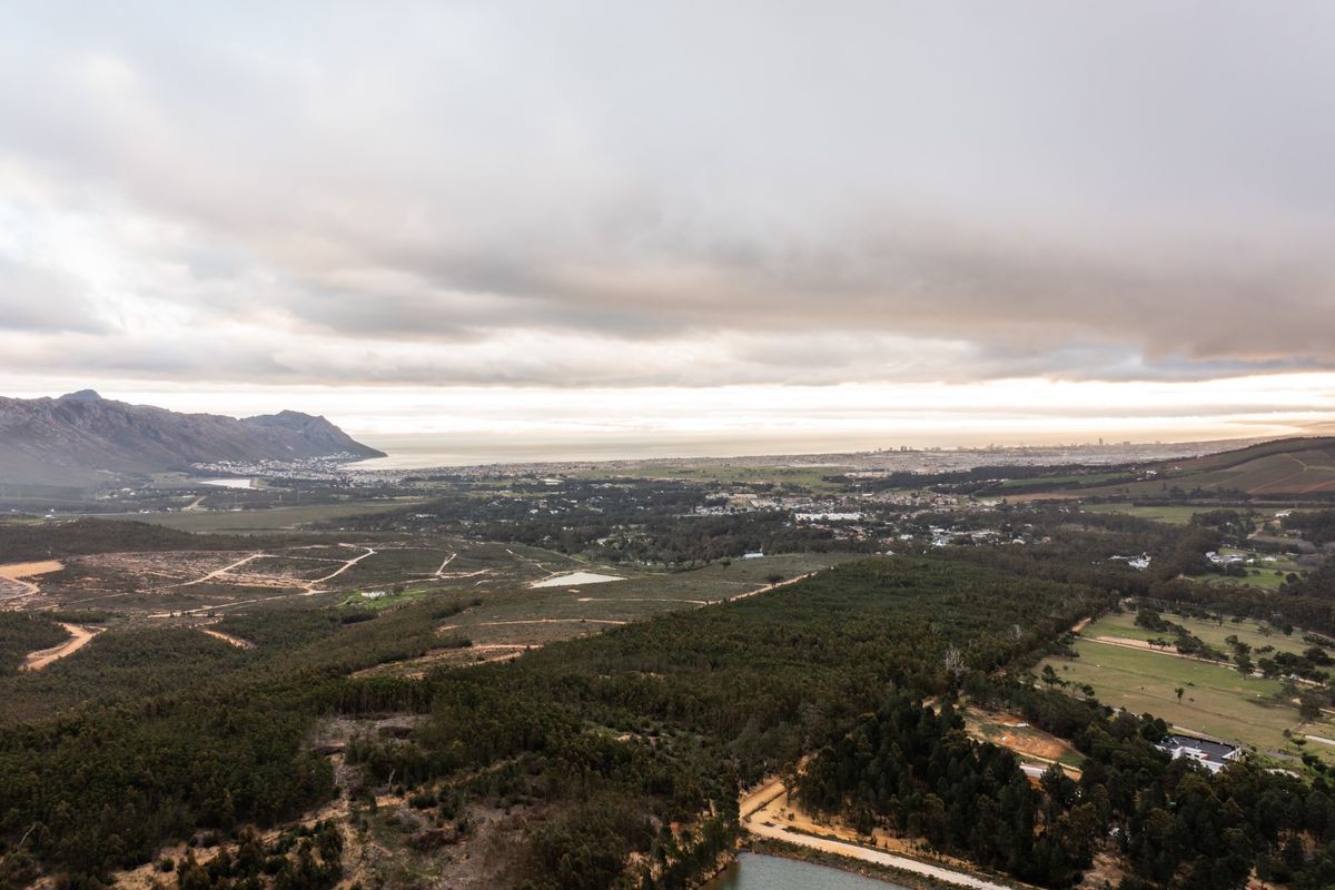 An expansive aerial view of the farm property, showcasing the surrounding landscape, distant mountains, and coastal horizon under a cloudy sky.