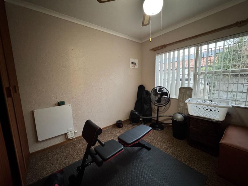 A functional bedroom featuring carpet flooring, a ceiling fan, and security bars on the window, currently utilized as a home gym space.