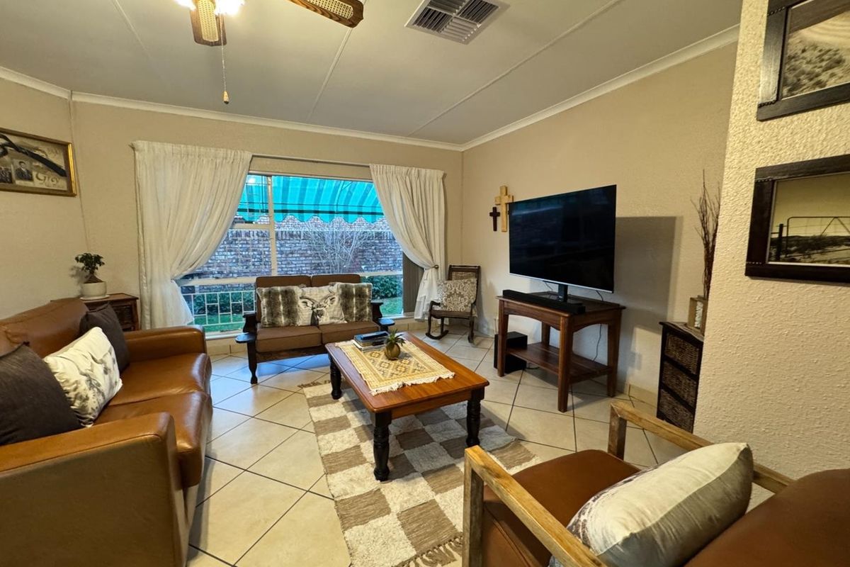 A comfortable living room featuring tiled flooring, a ceiling fan, and a large window providing natural light.