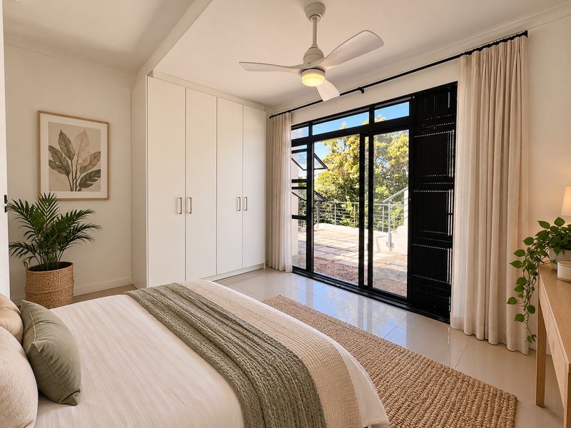 A bright, modern bedroom featuring built-in wardrobes, a ceiling fan, and large sliding glass doors that open onto an outdoor patio area.