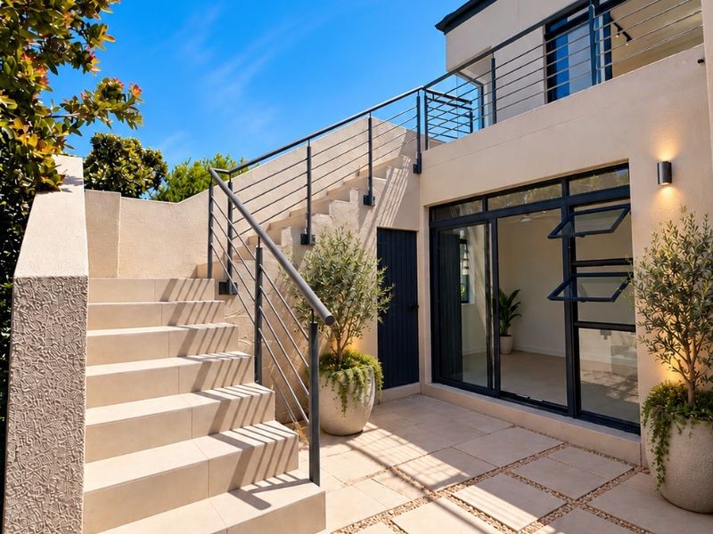 Modern paved patio area featuring a tiled staircase with metal balustrades, leading to an upper balcony and providing access to the interior living space.