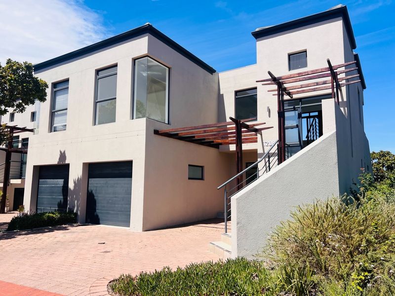 Modern double-story townhouse featuring a paved driveway, double garage, and a distinctive timber pergola over the entrance staircase.