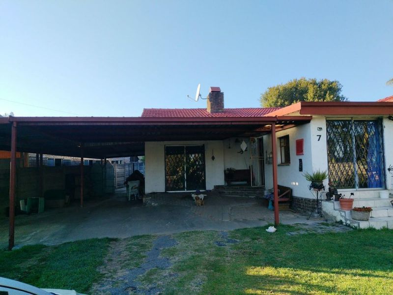 Front elevation of a single-story house featuring a large attached carport, tiled roof, brick chimney, and security gates at the entrance.