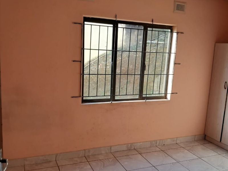A simple bedroom featuring tiled flooring, security bars on the window, and a built-in cupboard, offering a blank canvas for potential updates.