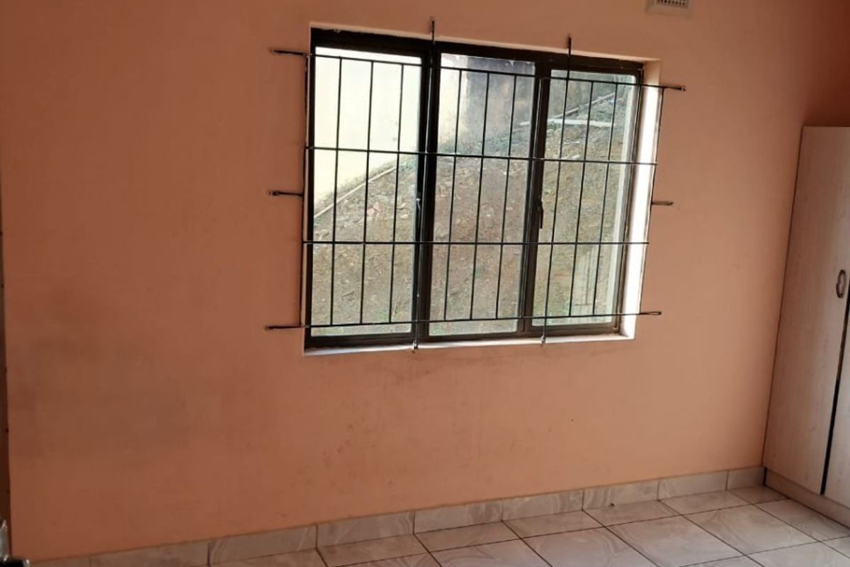 A simple bedroom featuring tiled flooring, security bars on the window, and a built-in cupboard, offering a blank canvas for potential updates.