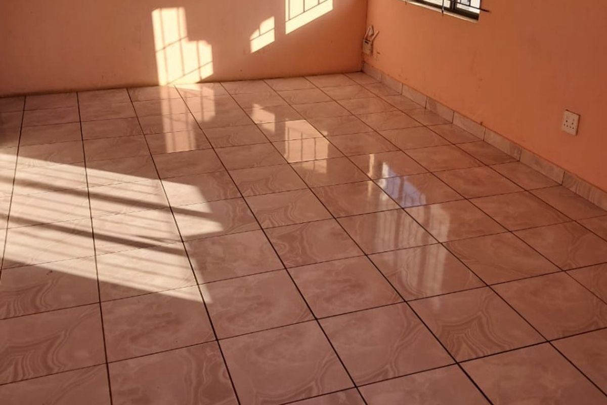 An empty living room featuring ceramic floor tiles, natural light, and security bars on the window.