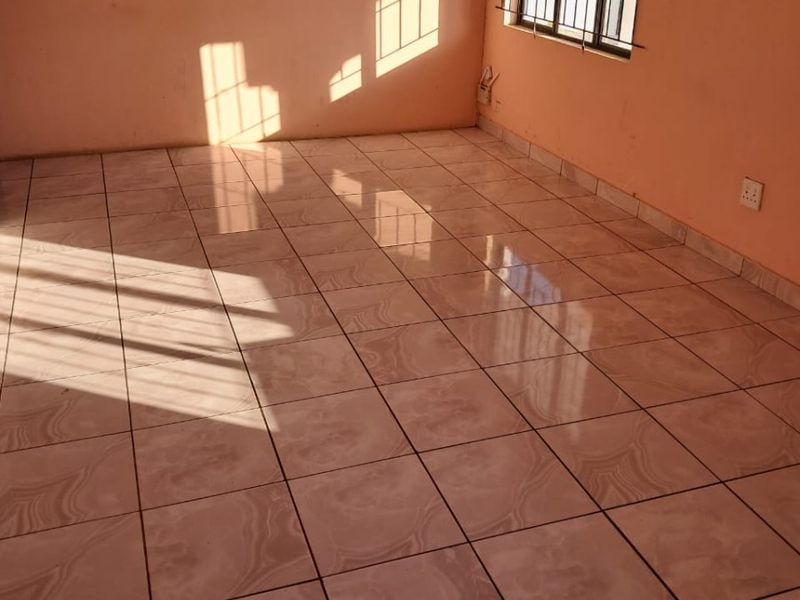 An empty living room featuring ceramic floor tiles, natural light, and security bars on the window.