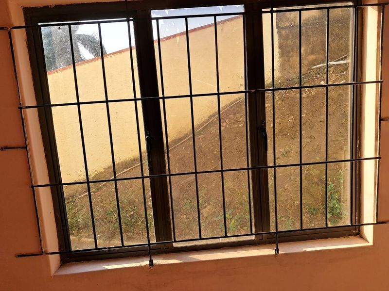 A close-up view of a window featuring dark aluminium frames and security bars, showing a visible crack in the glass pane.