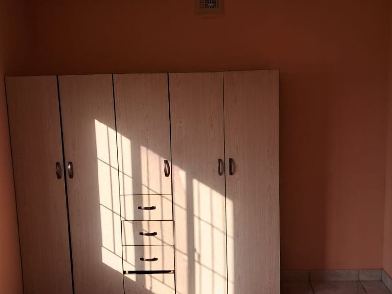 A bedroom featuring tiled flooring and a built-in wardrobe with integrated drawers, illuminated by natural light.
