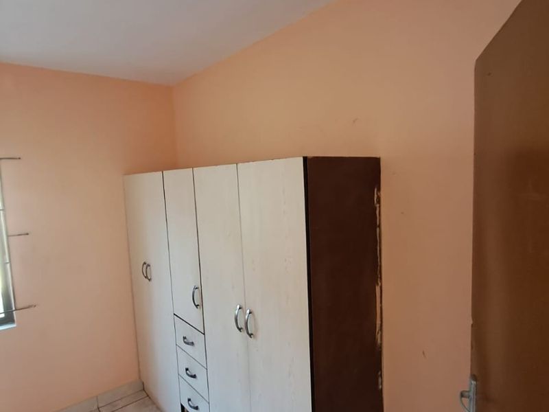 A bedroom featuring tiled flooring and a built-in wardrobe with visible wear on the side panel.