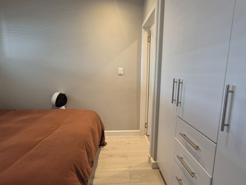 A well-maintained bedroom featuring modern laminate flooring and ample built-in cupboard storage with clean, neutral wall finishes.