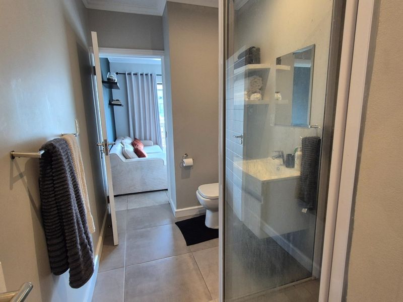 A modern bathroom featuring a wall-mounted vanity, glass shower enclosure, and tiled flooring, with a view through to the adjacent living area.
