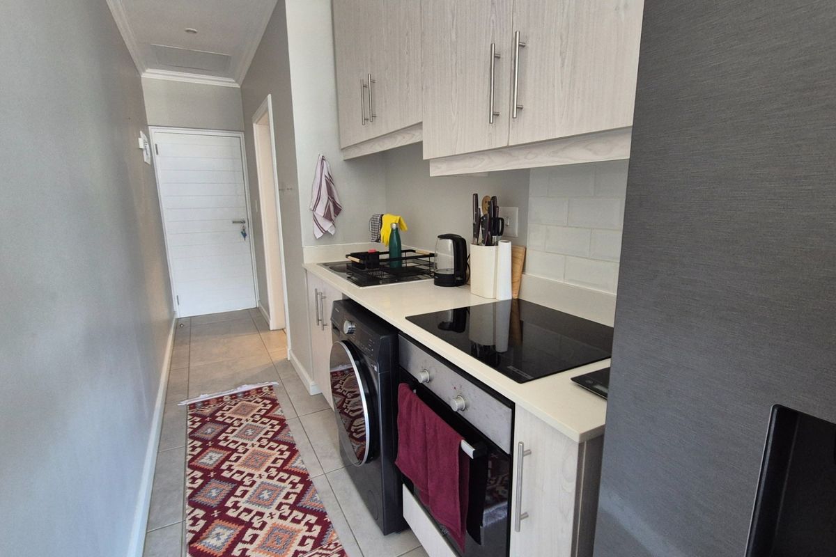A compact, modern kitchen featuring light wood-grain cabinetry, stone countertops, a subway tile backsplash, and integrated appliances including an electric hob and oven.