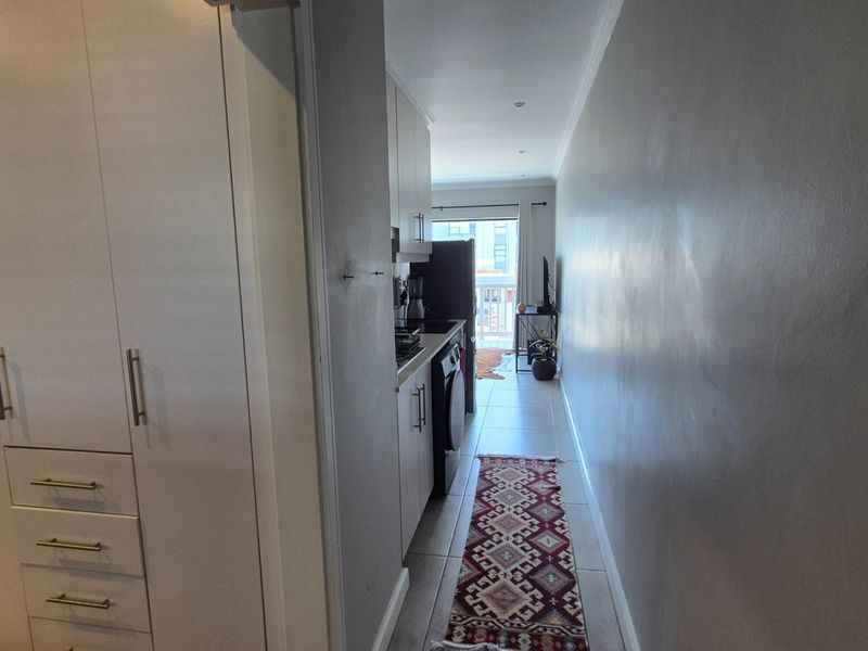 A functional hallway featuring built-in cabinetry and tiled flooring, leading towards an open-plan living area with natural light.