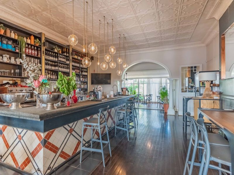 A well-appointed bar area featuring a tiled counter, extensive built-in shelving, elegant pendant lighting, and a classic pressed metal ceiling with hardwood flooring.