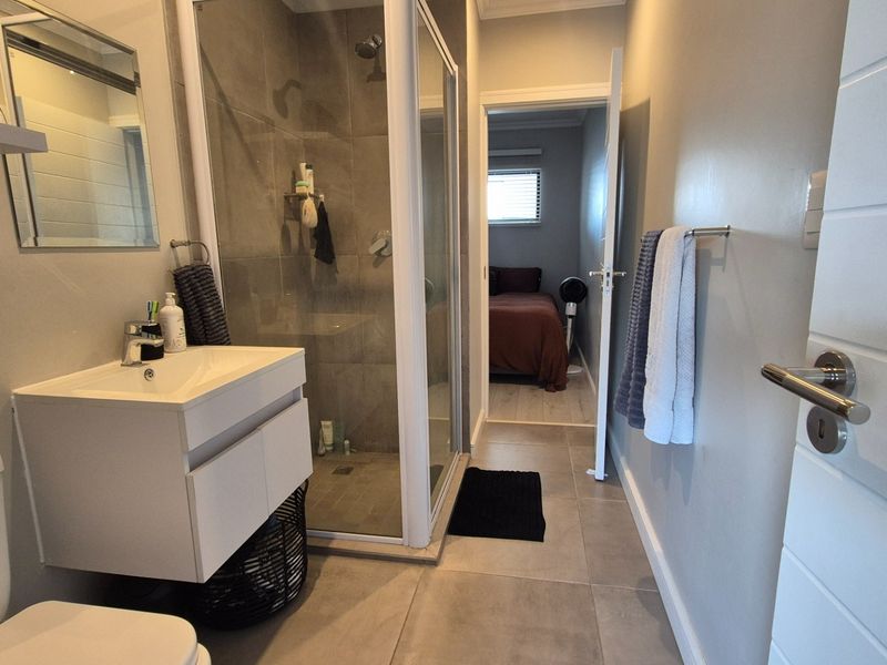 Modern bathroom featuring a wall-mounted vanity, glass-enclosed shower with tiled walls, and neutral ceramic floor tiling, offering a clean and contemporary aesthetic.