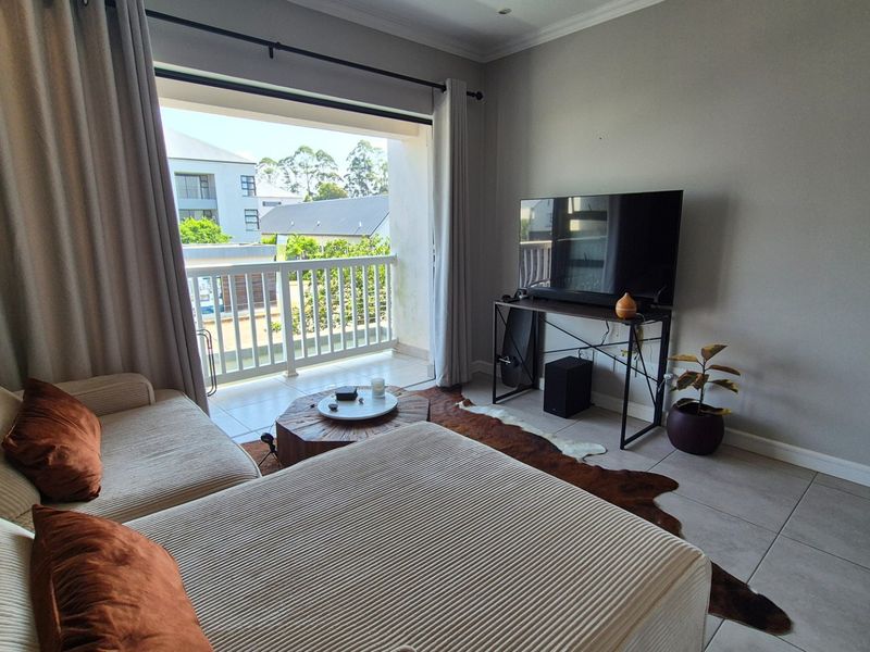 A bright living room featuring tiled flooring and a large sliding glass door that opens onto a private balcony.