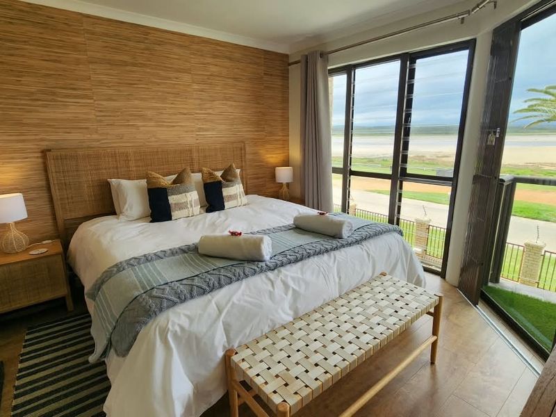 A well-appointed bedroom featuring wood-look wall paneling, laminate flooring, and large glass sliding doors that offer scenic views and access to the outdoors.
