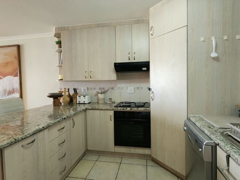 A functional kitchen featuring light wood-grain cabinetry, granite countertops, a built-in oven with hob, and tiled flooring, offering a clean and practical workspace.