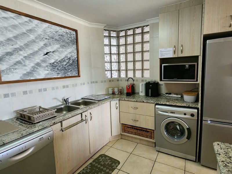 Functional kitchen featuring granite countertops, tiled backsplash, glass block window, and integrated appliances including a washing machine and dishwasher.