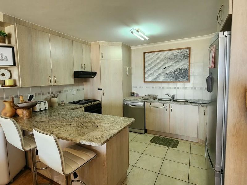 A functional kitchen featuring light wood-tone cabinetry, granite countertops, a double basin sink, and a built-in hob with an extractor fan.