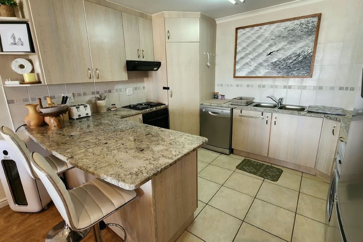 A functional kitchen featuring light wood cabinetry, granite countertops, a breakfast bar, and tiled flooring with a double basin sink and integrated extractor fan.