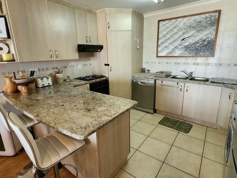 A functional kitchen featuring light wood cabinetry, granite countertops, a breakfast bar, and tiled flooring with a double basin sink and integrated extractor fan.
