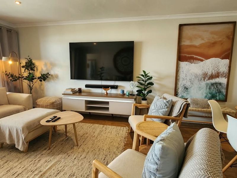 A bright and inviting open-plan living and dining area featuring timber flooring, recessed lighting, and a large sliding glass door leading to the outdoors.