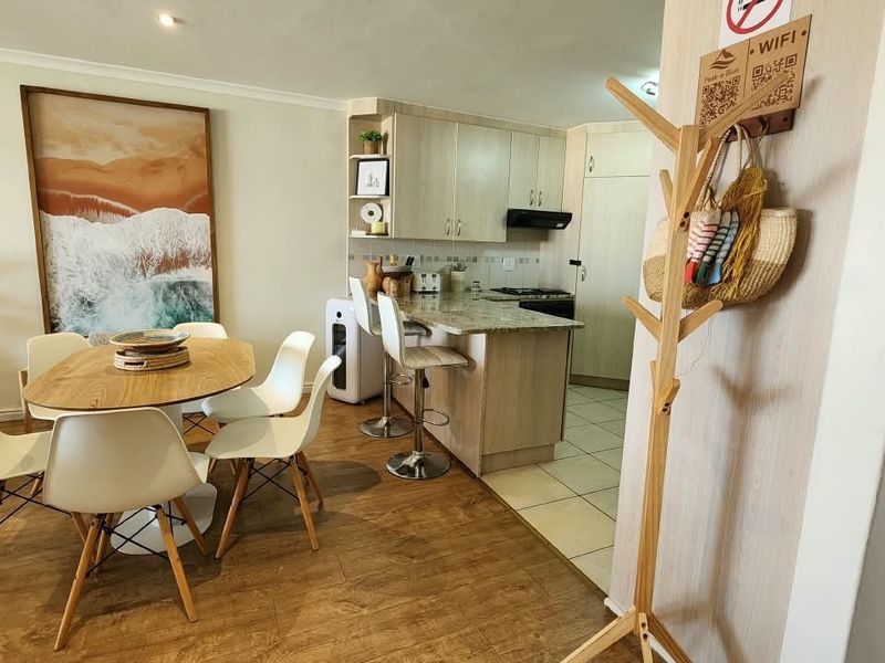 Open-plan living and dining area featuring a compact kitchen with granite countertops, built-in cabinetry, and a breakfast bar, finished with a mix of tile and laminate flooring.