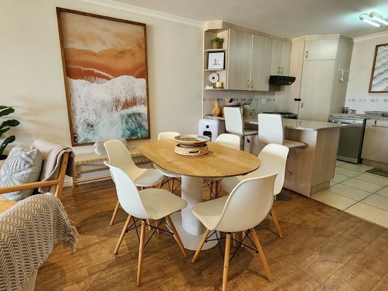 Open-plan living and dining area featuring laminate flooring, flowing into a functional kitchen with granite countertops, built-in cabinetry, and a breakfast bar.