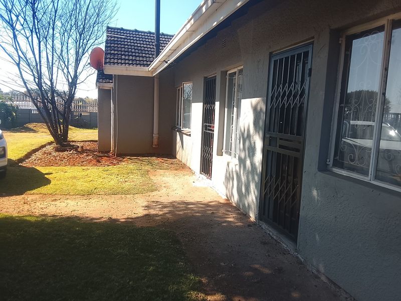 Rear exterior view of the house featuring a paved walkway, security gates, and a garden area with established trees.