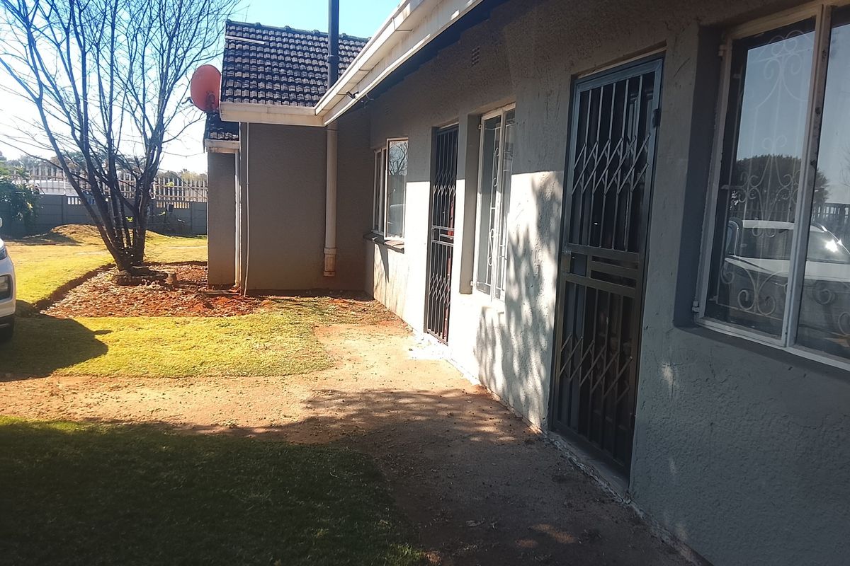 Rear exterior view of the house featuring a paved walkway, security gates, and a garden area with established trees.