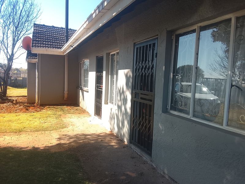 Rear exterior view of the house featuring a tiled roof, security gates on doors, and metal window frames with a surrounding garden area.