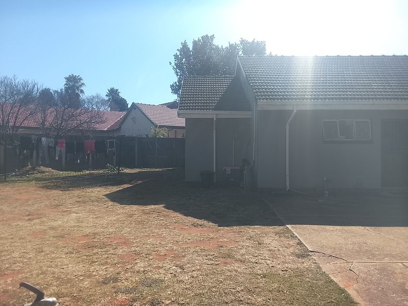 Rear view of the property showing a concrete driveway, tiled roof, and a spacious backyard area with perimeter walling.