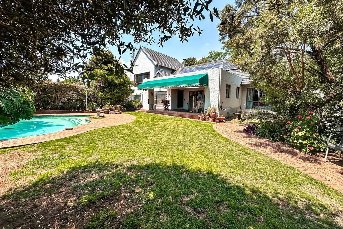 Rear view of the property featuring a landscaped garden, swimming pool, brick paved patio area, and solar panels installed on the roof.