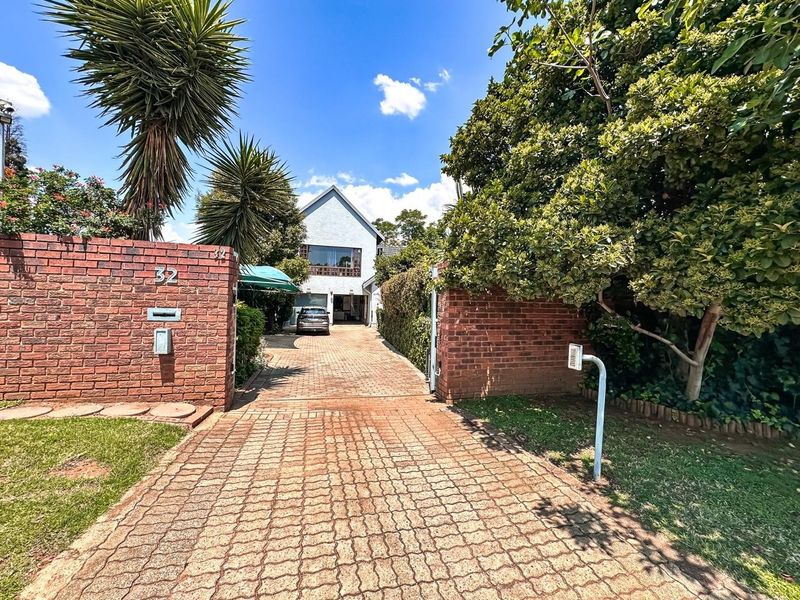 Front view of the property featuring a paved driveway, brick boundary walls, and established garden landscaping leading to the main residence.
