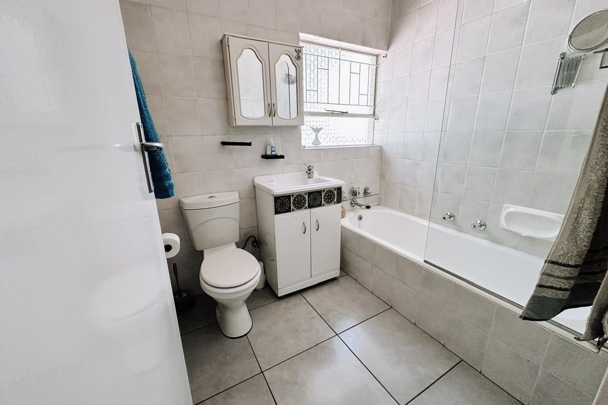 A functional bathroom featuring a tiled bathtub with a glass screen, a vanity unit with a basin, and a wall-mounted medicine cabinet.