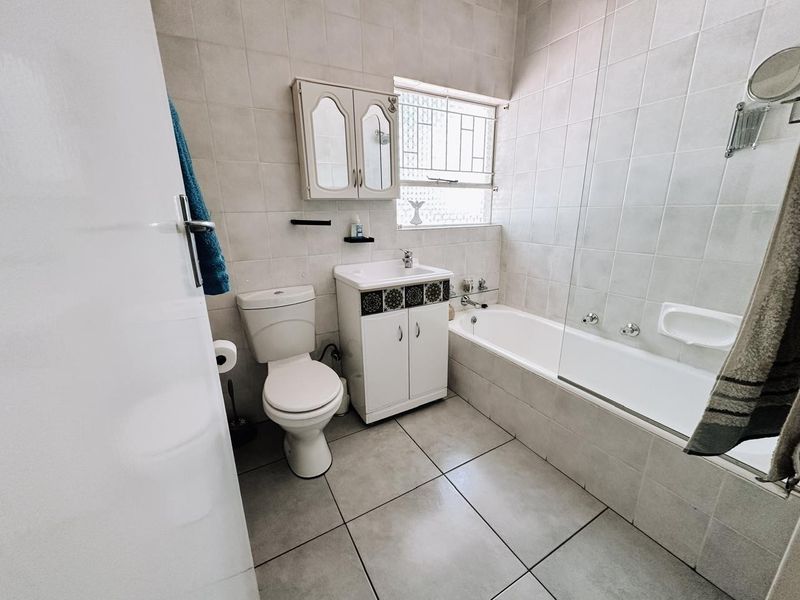 A functional bathroom featuring a tiled bathtub with a glass screen, a vanity unit with a basin, and a wall-mounted medicine cabinet.
