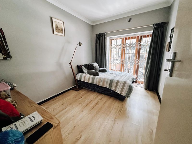 A well-lit bedroom featuring light-toned laminate flooring, cove cornicing, and a sliding glass door with integrated security gate providing access to the exterior.