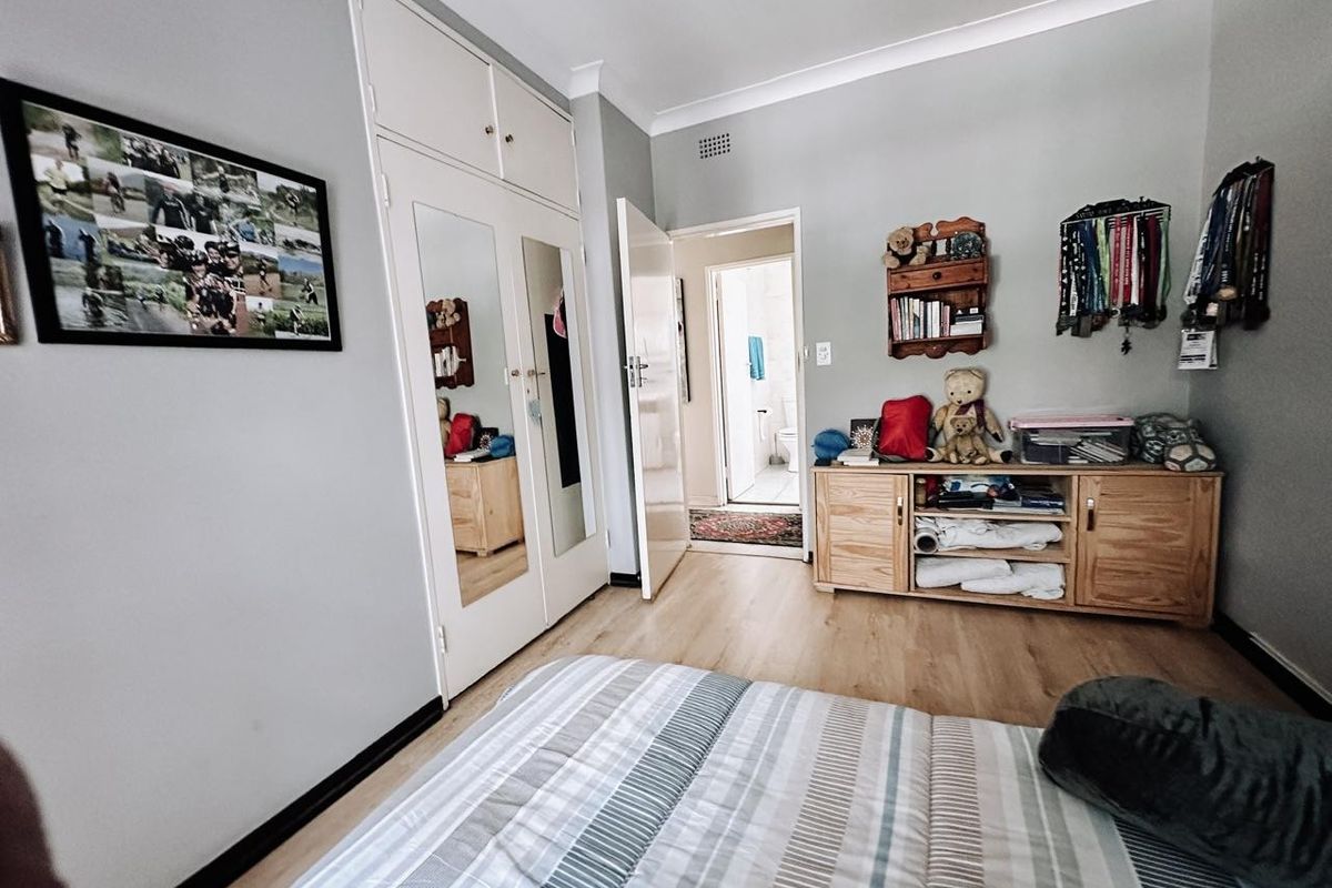 A bedroom featuring laminate flooring, built-in cupboards with mirrored panels, and direct access to an adjoining bathroom.