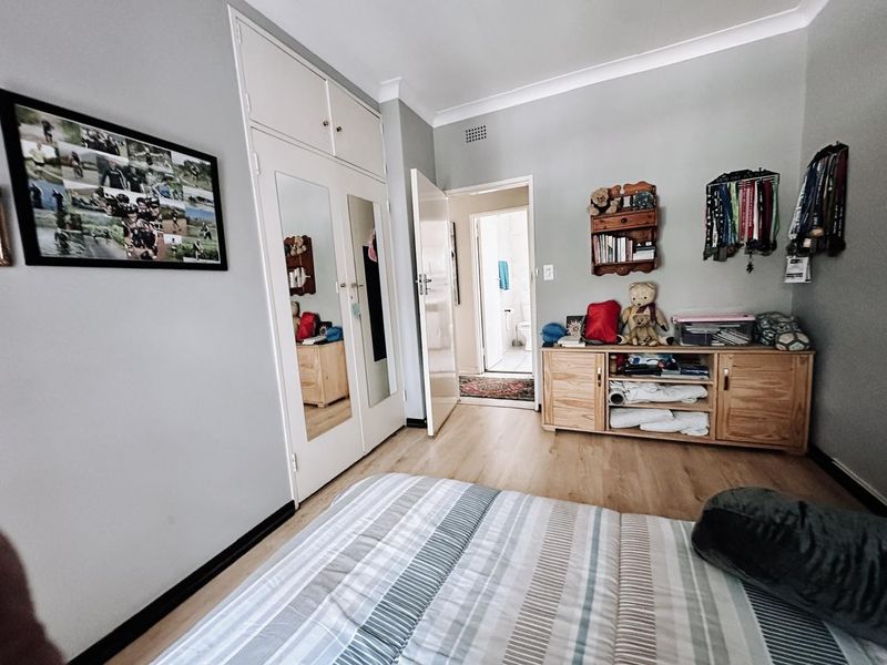 A bedroom featuring laminate flooring, built-in cupboards with mirrored panels, and direct access to an adjoining bathroom.