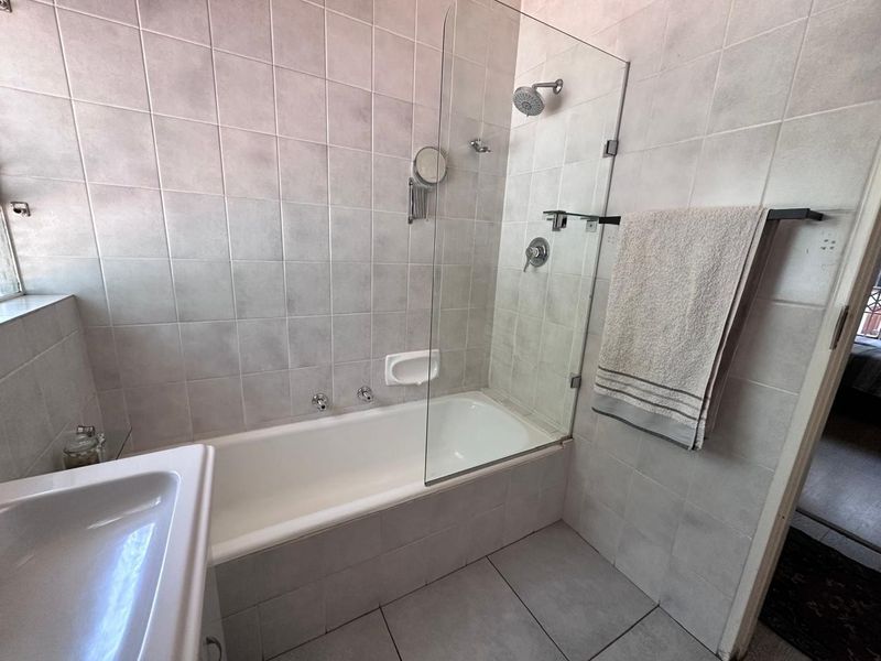 A functional bathroom featuring a built-in bathtub with a glass shower screen, wall-mounted shower fixtures, and neutral ceramic tiling throughout.
