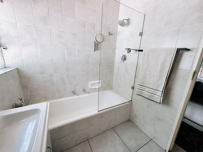 A functional bathroom featuring a built-in bathtub with a glass shower screen, neutral ceramic tiling, and modern chrome fixtures.