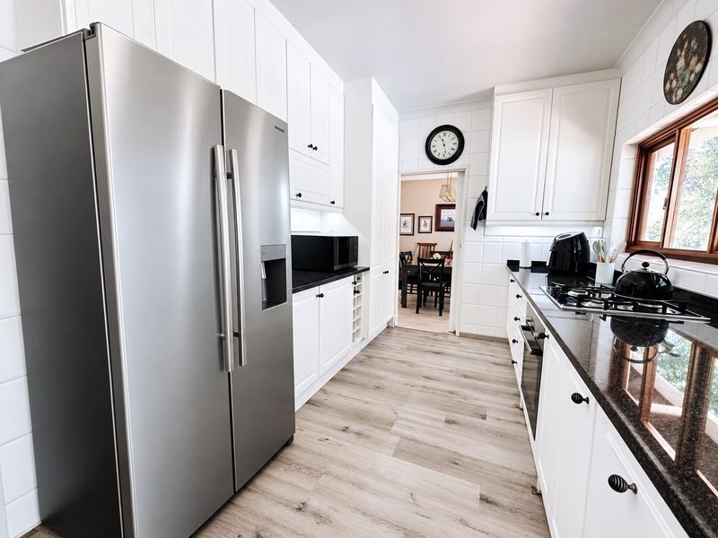 A well-maintained kitchen featuring white cabinetry, dark granite countertops, a gas hob, built-in oven, and modern laminate flooring.