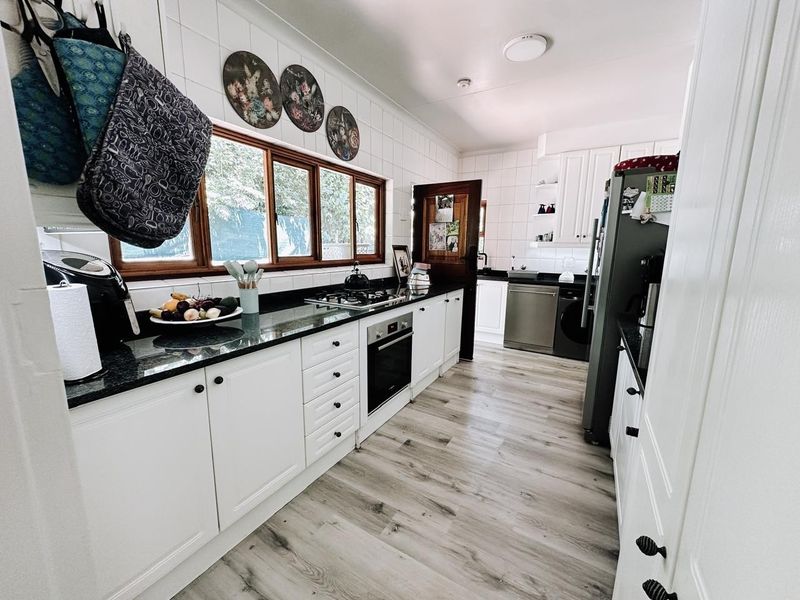 A well-maintained kitchen featuring white cabinetry, dark granite countertops, a gas hob, built-in oven, and modern laminate flooring with ample natural light.