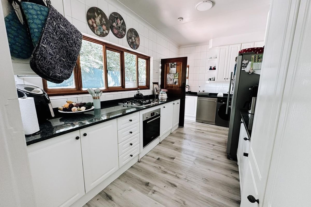 A well-maintained kitchen featuring white cabinetry, dark granite countertops, a gas hob, built-in oven, and modern laminate flooring with ample natural light.