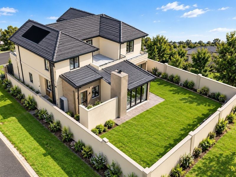 Aerial view of a modern two-story house featuring a tiled roof with solar panels, a private enclosed garden, and a paved patio area.
