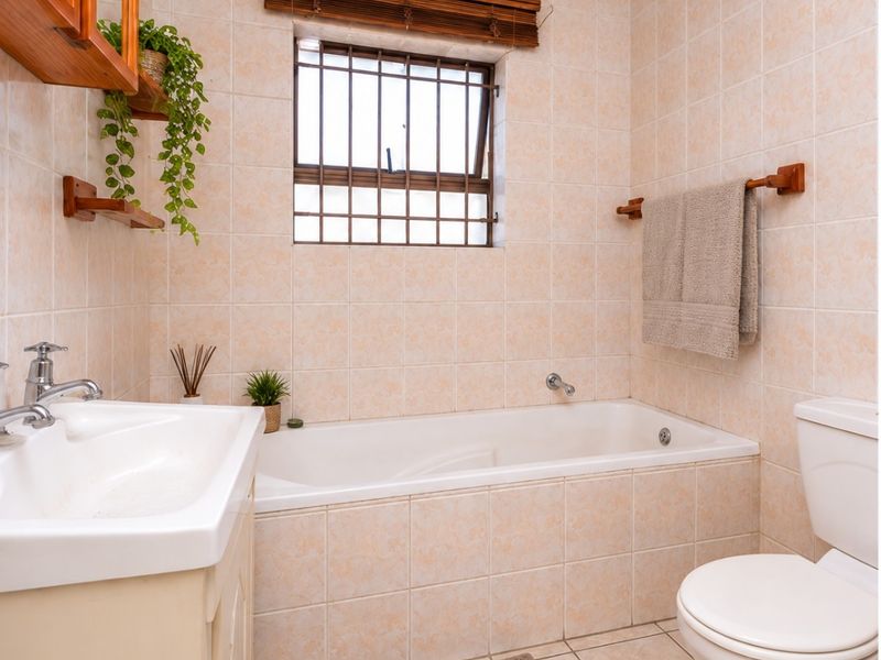 A functional bathroom featuring a built-in bathtub, vanity with basin, and neutral ceramic tiling throughout.